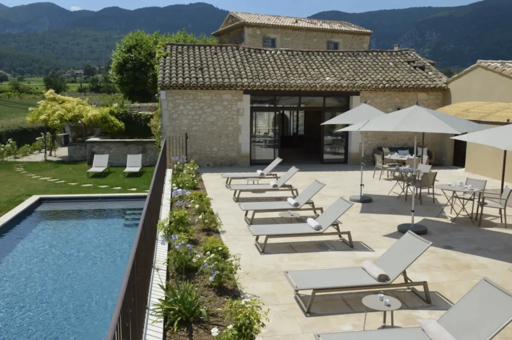 Aménagement paysager autour d’une piscine avec terrasse, massifs fleuris et maison provençale en pierre