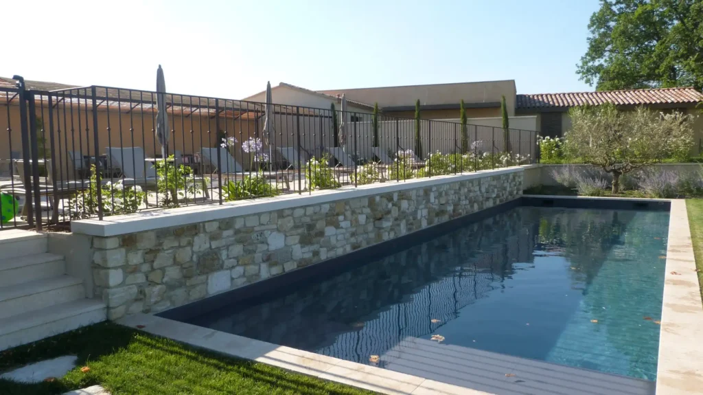 Piscine aménagée avec terrasse, massifs fleuris, olivier et muret en pierre dans un jardin provençal