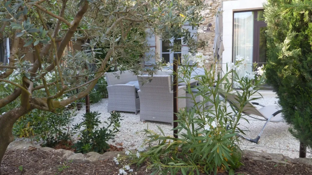 Coin détente aménagé dans un jardin méditerranéen avec olivier, lauriers fleuris et terrasse en gravier