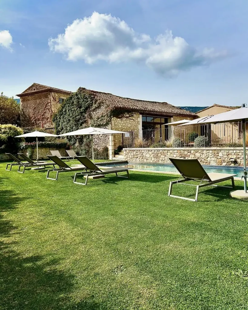 Jardin paysager avec piscine, pelouse et espace détente devant une bâtisse provençale en pierre
