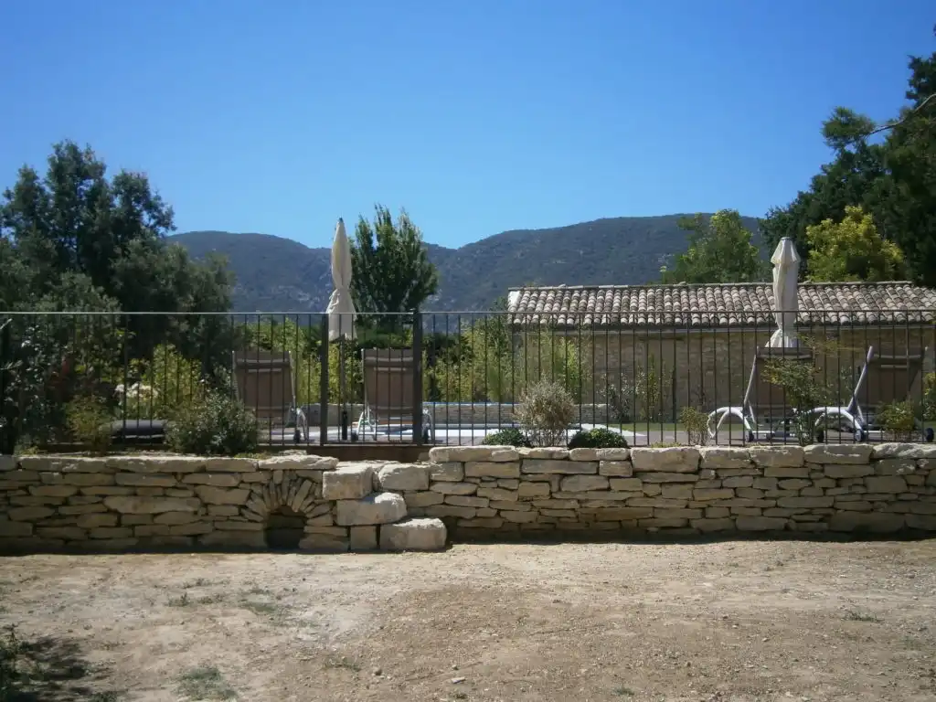 Jardin avec muret en pierre sèche, clôture en fer et piscine en arrière-plan