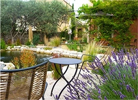 Terrasse de jardin avec table et fauteuils près d’un bassin entouré de plantes et lavande