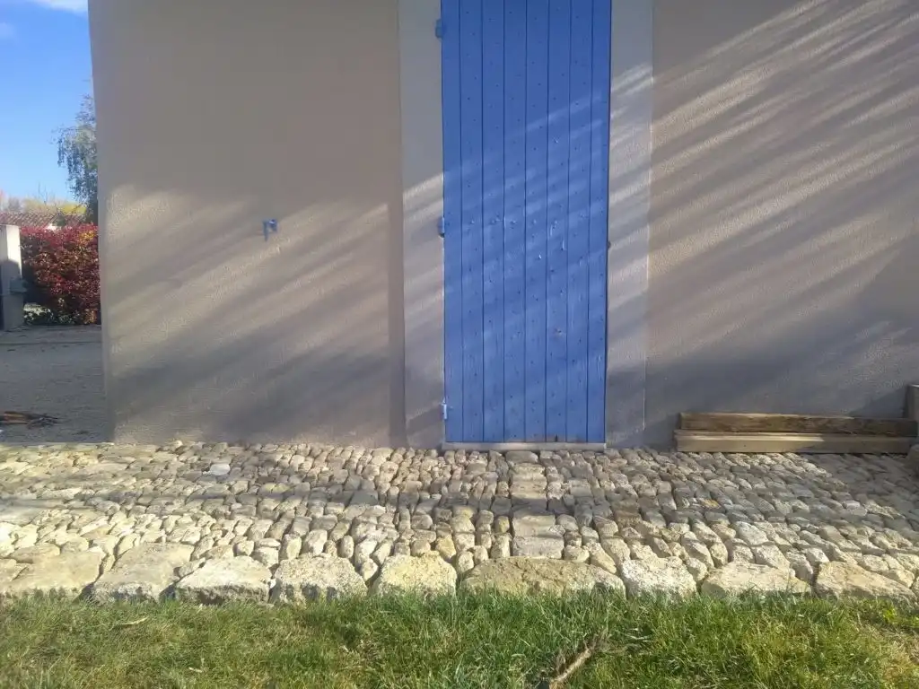 Pavage en pierre naturelle devant une maison avec porte bleue