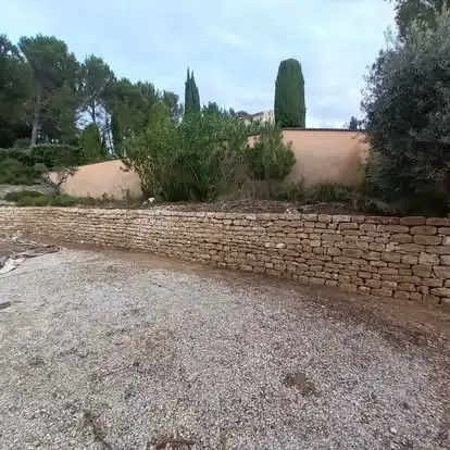 Mur de soutènement en pierre sèche à Velleron aménagé le long d’une zone de stationnement en gravier
