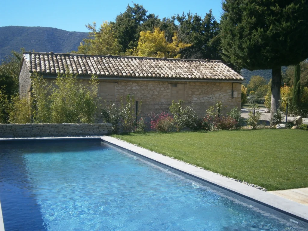 Piscine intégrée au jardin paysager de la Maison Magnarelle à Maubec avec pelouse, végétation et muret en pierre sèche