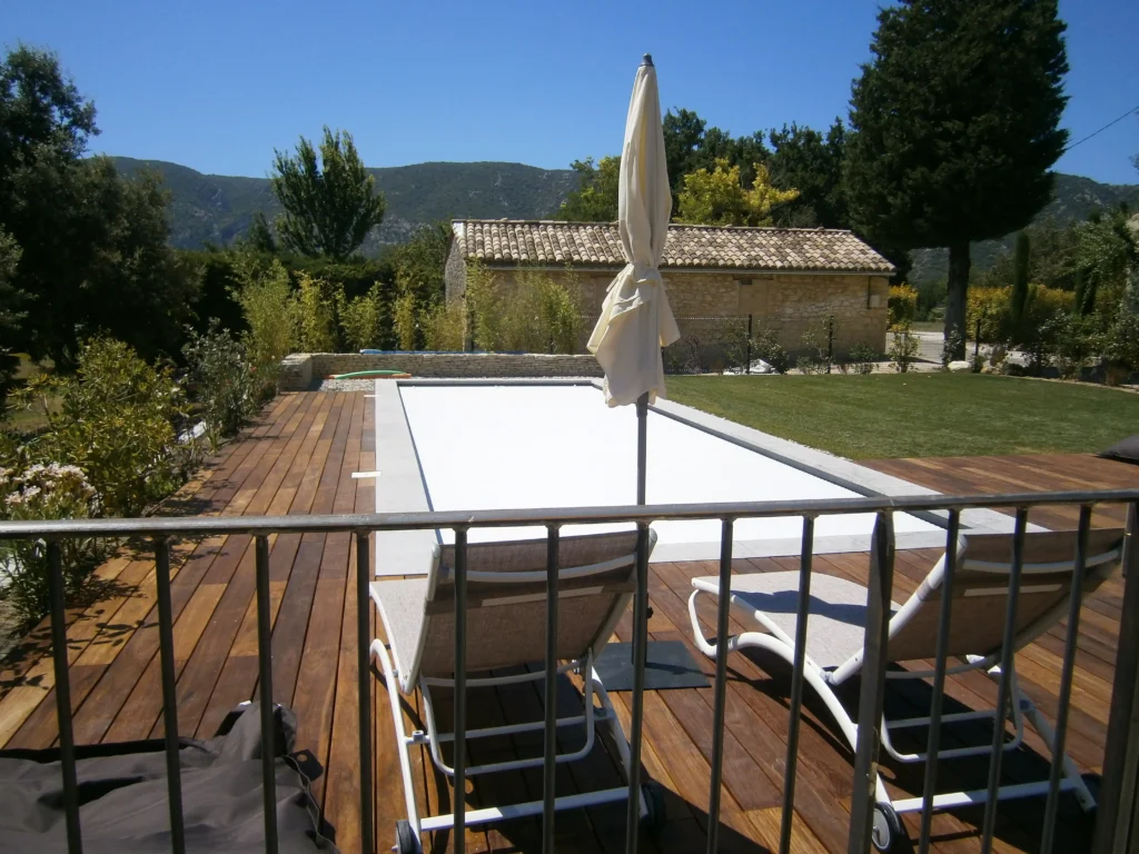 Terrasse en bois autour de la piscine de la Maison Magnarelle à Maubec avec jardin paysager et vue sur le Luberon